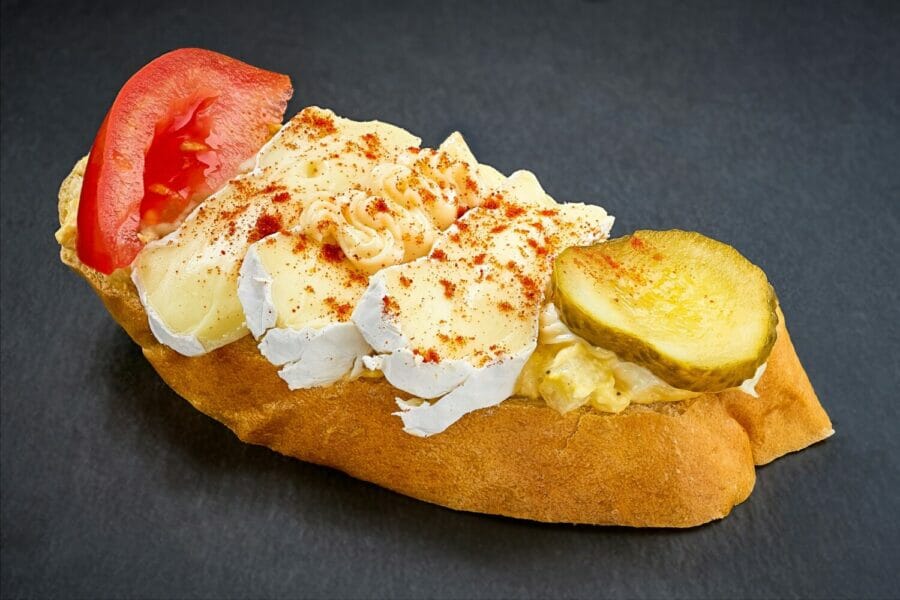 Weißbrot mit Brie, darunter feine Gemüsemayonnaise. Mit Tomaten und Essiggurke Dekoration.